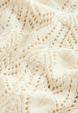 Țesătură tricotată crem cu un model texturat, de dantelă deschisă. Material moale, ușor, cu un design ondulat și cusături delicate, aerisite.