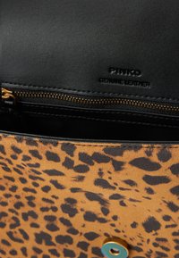 Borsa in pelle con stampa leopardata marrone e nera, dotata di chiusura a zip e hardware blu in accento. L'interno è in pelle nera di alta qualità.
