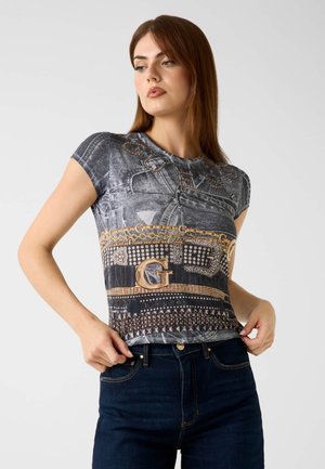 Korte mouw graphic t-shirt met een zwart en grijs patroon, versierd met gouden kettingaccenten en strass-details. Gecombineerd met donkerblauwe jeans.