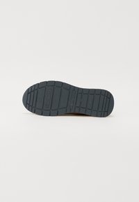 Svart gummisula med mönster och "Tom Tailor"-logotyp synlig, fotograferad mot en enkel vit bakgrund.