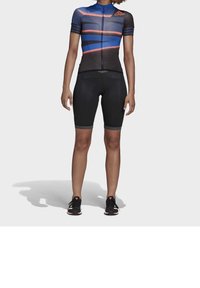 Pánský cyklistický dres s krátkým rukávem, modro-černý geometrický design, přední zip, v kombinaci s černými polstrovacími šortkami a černými teniskami.