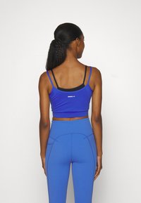 Zils sporta krass tops ar plānām siksniņām, apvienots ar augsto jostasvietu ziliem treniņbiksēm. Gluda tekstūra un diskrēts zīmols uz tops muguras.