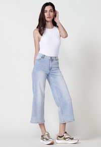Bodysuit blanco sin mangas combinado con jeans de pierna ancha color azul claro y zapatillas multicolor, mostrando un ajuste relajado y un estilo casual.