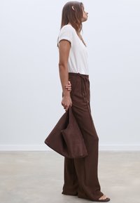 Bruna vida byxor med dragsko i midjan, kombinerade med en vit kortärmad skjorta och en brun mockaväska. Mjukt tyg material.