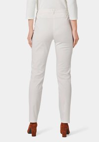 Lichtgrijze, slim-fit broek met een hoge tailleband, met een subtiele textuur. Draagt mooie, bruine schoenen met blokhak, gezien vanuit de achterkant.