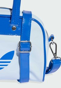 Torebka z lakierowanej skóry w kolorze niebiesko-białym o zaokrąglonym kształcie. Wyposażona w srebrne metalowe okucia, solidne paski oraz niebieski detal z logo.