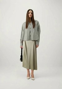 Striped black and white button-up shirt with a pocket, paired with a smooth, light olive green midi skirt and cream high heels.
