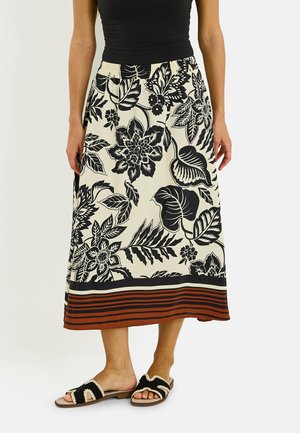 Mujer con falda midi crema con estampado floral negro y bajo a rayas en color óxido, combinada con top negro sin mangas y sandalias negras.