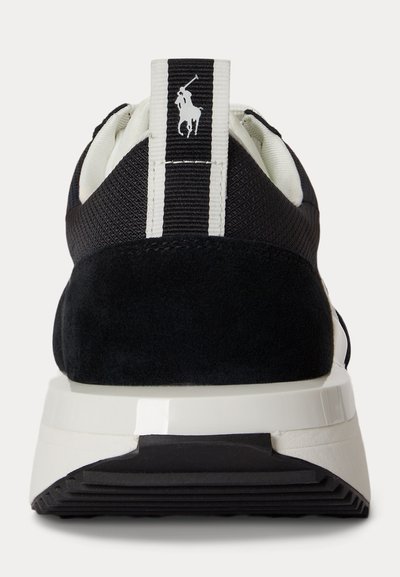 Baskets noir et blanc vues de derrière, montrant un talon texturé, une semelle blanche et une languette verticale avec un logo joueur de polo blanc.