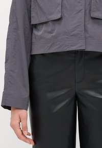 Gray, lightweight jacket with a cropped design and two large front pockets, paired with shiny black faux leather pants.