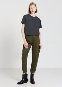 Schwarzes Kurzarm-T-Shirt, olivgrüne Cargo-Hosen mit Seitentaschen und schwarze Knöchelstiefel. Einfaches Design mit lässiger Passform.