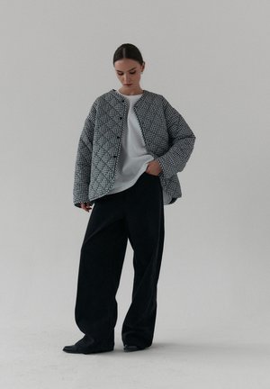 Kurtka w czarno-białą, pikowaną kraciastą siatkę z okrągłym dekoltem i zapięciem na guziki, noszona na białej koszuli, w zestawieniu z czarnymi spodniami o szerokich nogawkach.