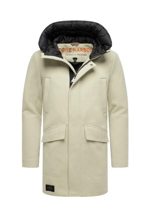 Manteau à capuche crème avec doublure noire, deux poches avant et une texture lisse. Présente un patch logo à l'ourlet et une fermeture à bouton pression.