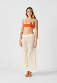 Haut court orange avec des bords blancs associé à un pantalon en crochet blanc ample avec un motif en grille. Pas de chaussures.