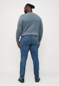 Blauwe denim jeans met een slim fit, voorzien van achterzakken en een tan leren label op de tailleband, gecombineerd met een lichtblauw overhemd met lange mouwen.