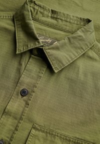 Oliwkowa koszula na guziki z kołnierzykiem, czarnymi guzikami, kieszenią na piersi oraz subtelną pionową teksturą w paski.