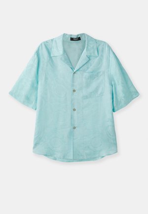 Una camisa de manga corta azul claro hecha de tela suave, que presenta un cuello extendido, un bolsillo delantero y un sutil patrón texturizado, con botones dorados.
