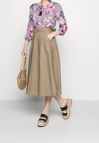 Bluzka w kwiatowy wzór z rękawami 3/4, połączona z beżową spódnicą do kostek z kieszeniami. Czarne sandały na platformie z paskami.