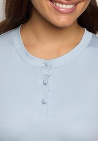 Světle modrá košile s krátkým rukávem a kulatým límečkem, se třemi knoflíkovými zapínáními a hladkým textilním povrchem.