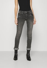 Harmaat farkut, joissa on kapea istuvuus ja kevyttä haalistumista, viisi taskua, käännetyt lahkeet ja vyölenkit, yhdistettyinä mustiin koroketossuihin.