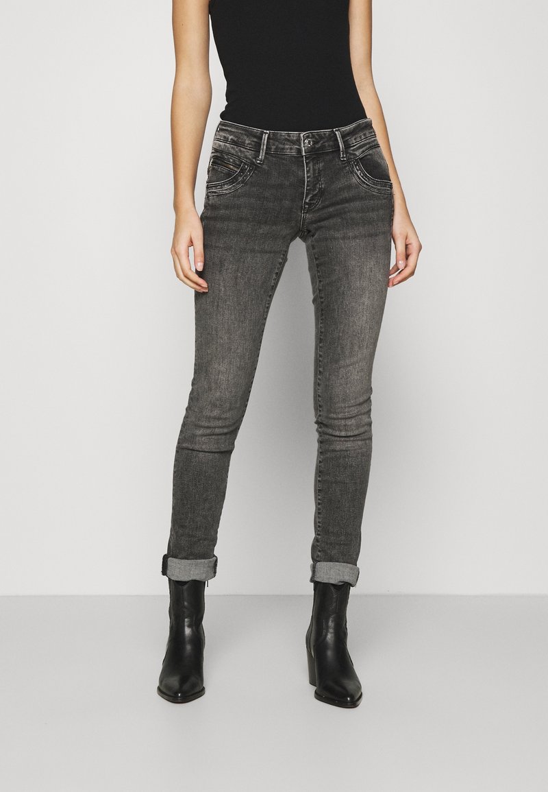 Harmaat farkut, joissa on kapea istuvuus ja kevyttä haalistumista, viisi taskua, käännetyt lahkeet ja vyölenkit, yhdistettyinä mustiin koroketossuihin.