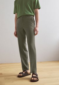 Calças claras verde-oliva com um corte ajustado, combinadas com umas sandálias castanhas escuras com fivelas e sola de cortiça.