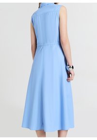 Jasnoniebieska, bezrękawnikowa sukienka z kołnierzykiem, elastycznym pasem i rozkloszowanym dołem, uszyta z gładkiego, lekkiego materiału.