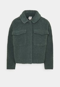 Grøn fleecejakke med krave. Har to brystlommer og en firkantet form. Tekstureret stof med et blødt, fluffy udseende.