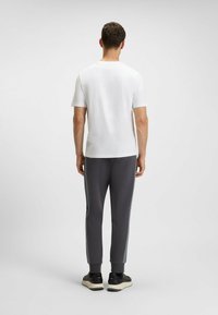 White short-sleeve T-shirt paired with dark gray tapered joggers featuring side stripes, ribbed cuffs, and black sneakers.