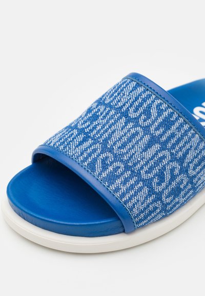Blå sandaler med glidelås og vevd overdel som har et teksturert mønster og solid blå stropp. Sålen er hvit med en glatt finish.