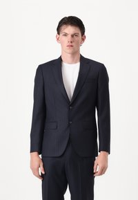Marineblau gestreifter Anzug mit zwei Knöpfen, Reverskragen und seitlichen Taschen. Glatte Stoffstruktur, taillierte Passform, weißes Innenhemd sichtbar.