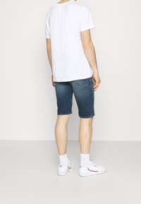 Pantalones cortos de mezclilla en un lavado medio con dobladillos enrollados, combinados con una camiseta básica de algodón blanca y zapatillas blancas. Presenta un diseño y ajuste sencillo.