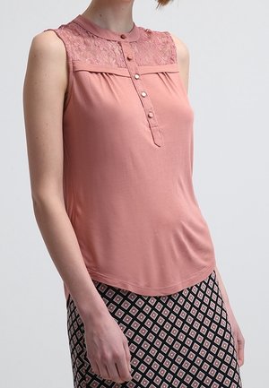 Mouwloos roze topje met kanten inzetstuk en knopen aan de voorkant, gedragen met een geplooide rok met diamantvormen.