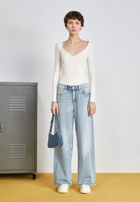 Body bianco a maniche lunghe con scollatura torcigliona, abbinato a jeans a vita alta a gamba larga di colore azzurro chiaro. Completato con una piccola borsa in denim.