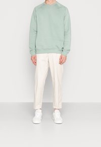 Felpa verde chiaro con colletto tondo, polsini e orlo a coste. Abbinata a pantaloni beige, larghi e comodi, e sneaker bianche.