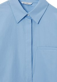 Camicia azzurro chiaro con colletto realizzata in tessuto morbido, dotata di chiusura a bottoni e di una tasca sul petto, con dettagli di cucitura discreti.