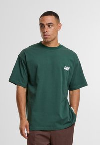 Green cotton t-shirt with a relaxed fit, short sleeves, a crew neckline, and a small white logo on the left chest.