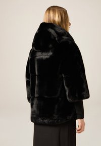 Czarna peleryna z sztucznego futra z szerokimi rękawami, wysokim kołnierzem i miękką teksturą. Charakteryzuje się pudełkowym kształtem i gładkim wykończeniem.