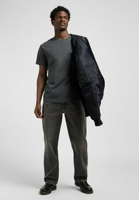 Camiseta gris oscuro combinada con jeans oscuros, sosteniendo una chaqueta bomber azul marino. Textura suave, corte relajado, costuras detalladas en la camiseta y la chaqueta.