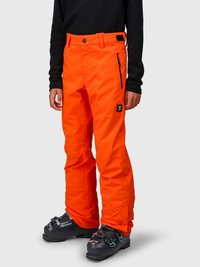 Person iklædt lys orange skibukser med lynlåslomme i siden og sorte ski støvler, stående foran en ensfarvet baggrund.