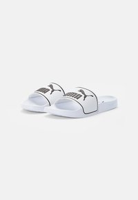 Biele šľapky s textúrovaným popruhom a čiernym brandingom PUMA, ponúkajúce plochú podrážku a otvorený dizajn špičky.