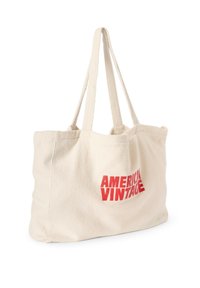 Sac tote en toile de couleur crème avec une texture douce. Présente un texte imprimé rouge "AMERICAN VINTAGE." Longs anses pour un transport facile.