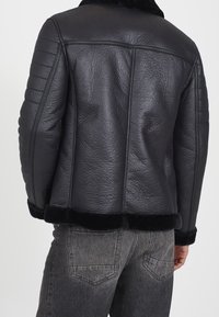 Giacca in pelle nera con finitura texturizzata, caratterizzata da colletto e polsini in pelliccia, design imbottito sulle maniche e una silhouette aderente.