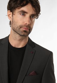 Dunkelgrauer Blazer mit subtiler Textur, einem burgunderfarbenen Akzentknopf und einer kastanienbraunen Einstecktuch über einem schwarzen T-Shirt.