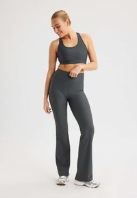 Grijze geribbelde sportbeha en uitlopende leggings, met een hoge tailleband en rekbare stof. Model draagt sportchoenen.