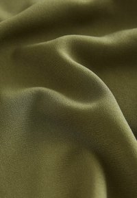 Un tissu vert olive présente une surface lisse, légèrement texturée avec des plis doux, mettant en valeur son tombé léger et fluide.