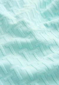 Tissu bleu clair avec un motif texturé en relief composé de formes "T" entrelacées répétées en rangées diagonales.