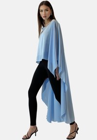 Ljusblå genomskinlig cape-topp med flödande design, kombinerad med svarta leggings och svarta spänningstossor. Slät struktur, minimalistisk stil.