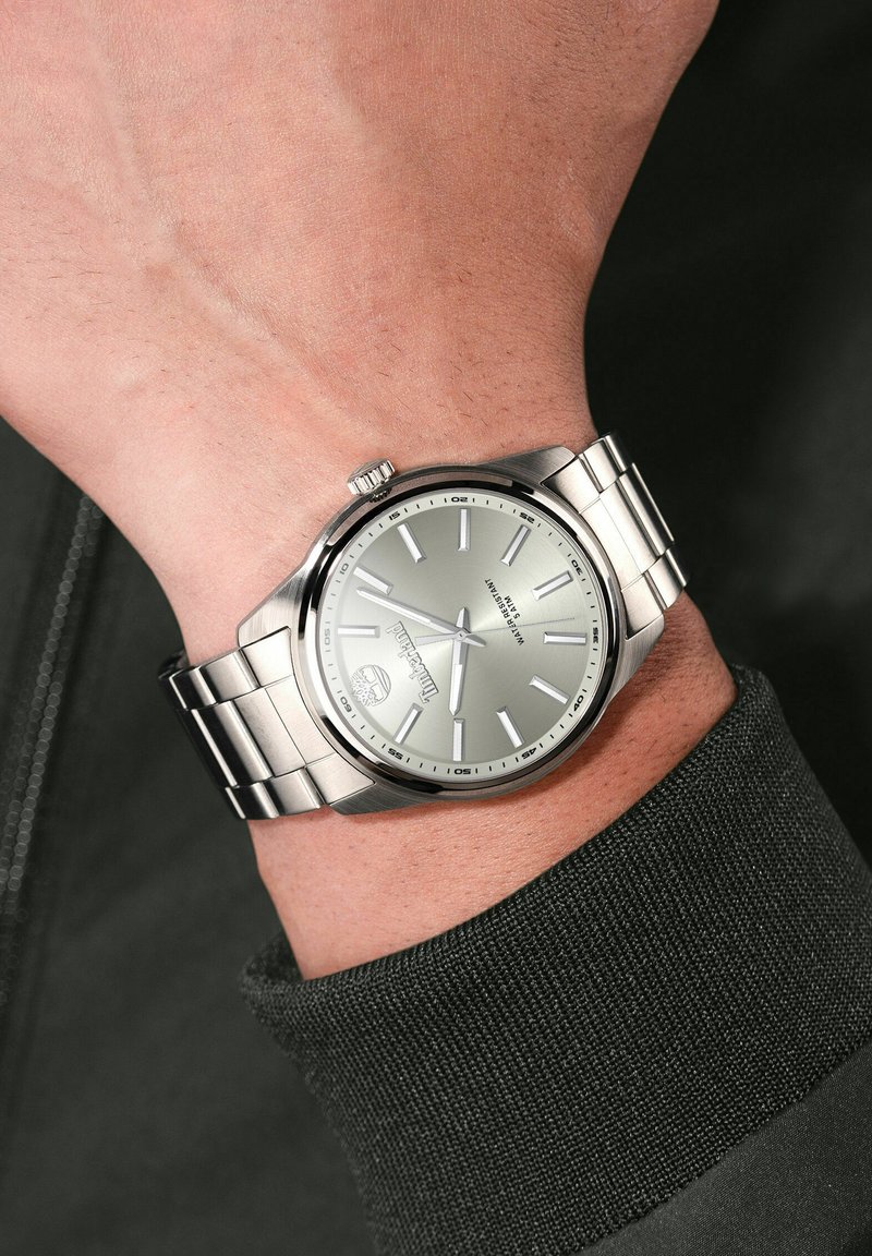 Orologio in acciaio inossidabile argento con quadrante di un grigio metallico, indicatori delle ore argentati e bracciale. Corona distintiva alle 3.