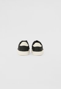 Czarne sneakersy z kontrastującymi białymi podeszwami i akcentami. Teksturowany materiał, niski krój i zaokrąglony uchwyt na pięcie dla łatwego zakładania.